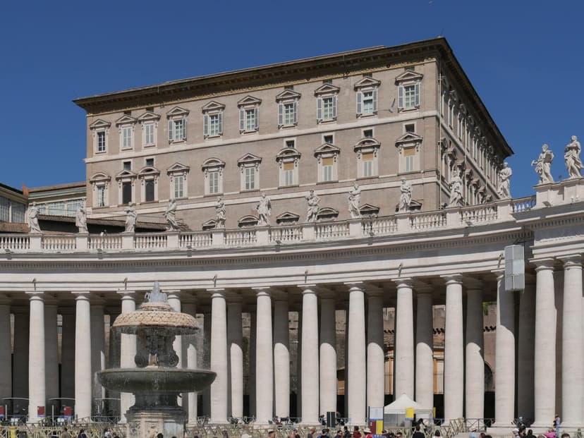 A quiet plaza with the Vatican exterior wall and a modern digital screen visible simultaneously