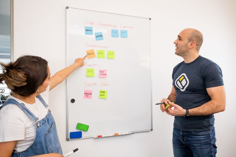 A small export team of two people reviewing a whiteboard with a 4-week content plan, pointing at sticky notes organized by buyer persona