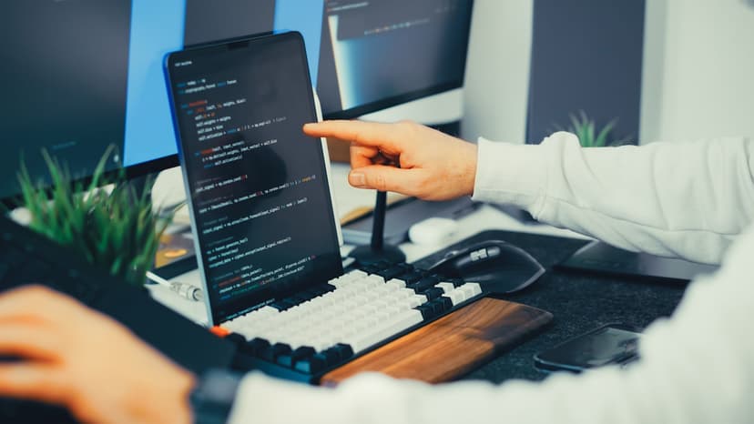 Seseorang yang tampak seperti senior developer membuka banyak tab di layar dan fokus memeriksa kode, sementara kursi-kursi di sekitarnya kosong
