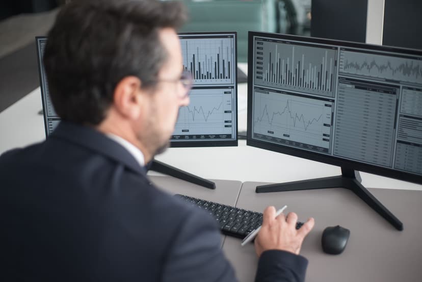 A focused South Korean export sales manager sitting at a desk with two monitors, comparing a printout datasheet with on-screen CRM data under warm office lighting.